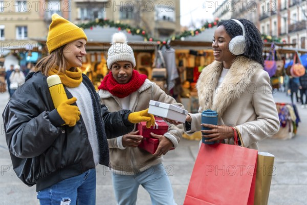 Happy friends exchanging gifts and enjoying hot drinks at a christmas market during winter holidays