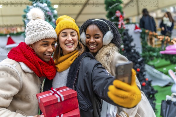 Happy multi ethnic friends taking a selfie at a christmas market, holding presents and shopping bags