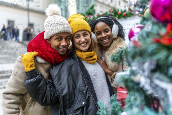 Happy multi ethnic friends enjoying christmas city during winter holidays, wearing winter clothes and smiling near a decorated christmas tree