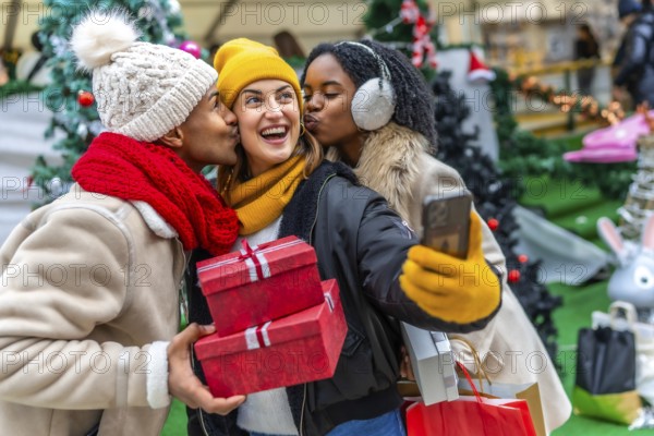 Three happy friends kissing a girl holding christmas gifts and taking a selfie at a christmas market