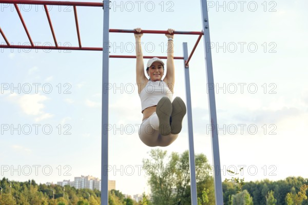 A woman is engaging in a fitness routine by performing pull-ups on a red metal bar at a park