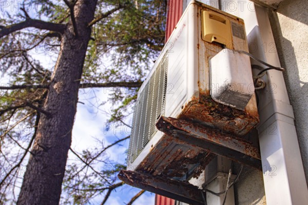 An old and rusty air conditioner hanging on the hotel building, in the sunny outdoor, seaside resort