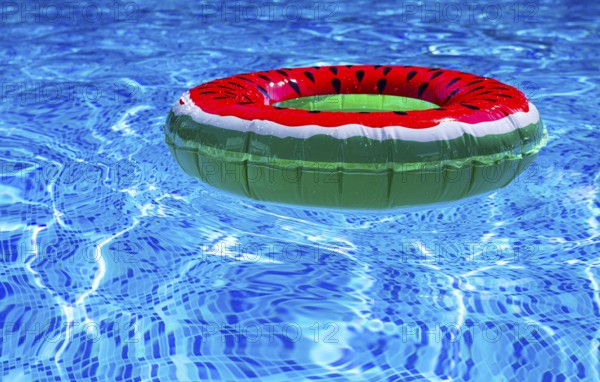 A bright ring-a float, with a watermelon, in the clear blue water of the pool, under the sunlight