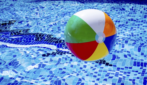 Colorful beach ball floats on the surface of a pool reflecting sunlight on a summer day