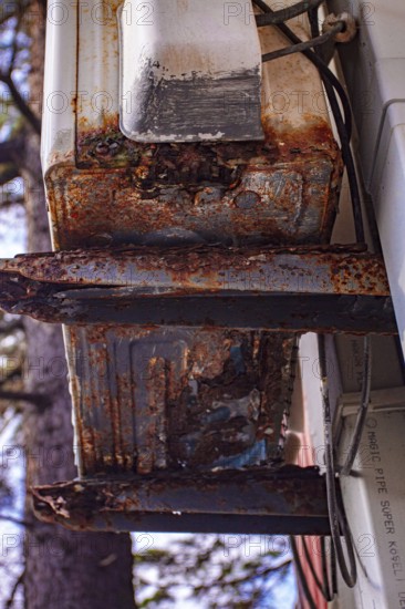 An old and rusty air conditioner hanging on the hotel building, in the sunny outdoor, seaside resort
