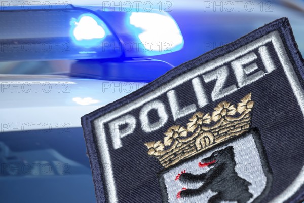 (Photomontage) Symbolic image of a police operation in Berlin: Berlin police emblem in front of flashing blue lights
