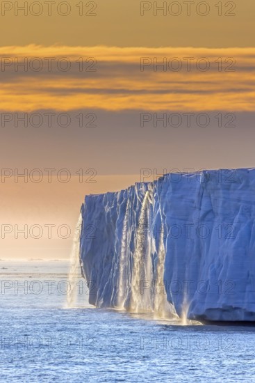 Waterfall at edge of Brasvellbreen glacier from the ice cap Austfonna pouring into the Barents Sea at sunset, Nordaustlandet, Svalbard, Spitsbergen