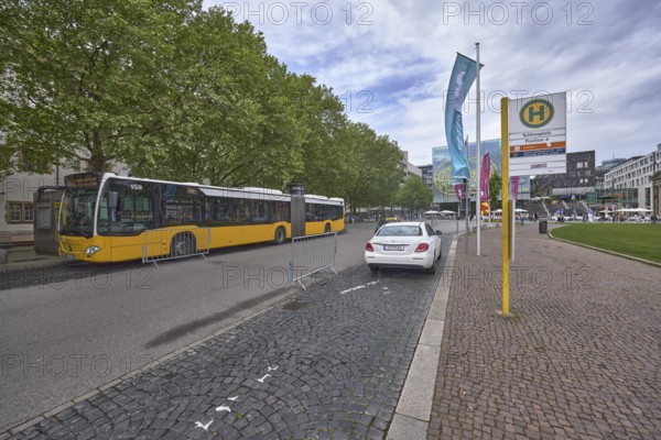 City centre, bus stop Schlossplatz, street, pavement made of cobblestones, public bus, taxi, general architecture, flags on flagpoles, trees, milky blue sky, diffuse light, Königstraße, Stuttgart, state capital, city district Stuttgart, Baden-Württemberg, Germany