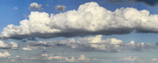 Stratocumulus cloud in the centre of the picture, dense cloud cover of many different cumulus clouds in the background, bright blue sky above, international