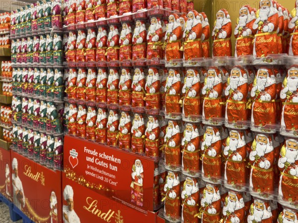 Display in shelf of wholesale of chocolate Santas Father Christmases Chocolate Father Christmases in different colours of staniol paper of chocolate brand Lindt arranged like army of Father Christmas, Germany