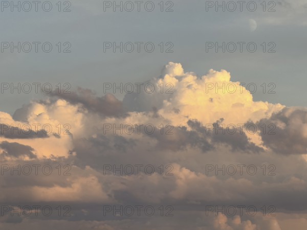 Mystical impression of cumulus cluster clouds at dusk illuminated by warm light, in the background at the top of the sky crescent moon in haze, international
