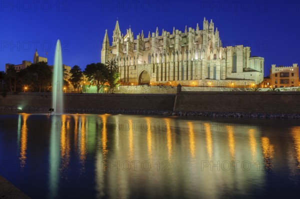 Night shot atmospheric photo in blue hour of Cathedral of Saint Mary of the Holy Mary Episcopal See La Seu, in front artificial lake water basin in Parc de la Mar with fountain fountain reflection on water surface, Palma de Majorca, Majorca, Balearic Islands, Spain