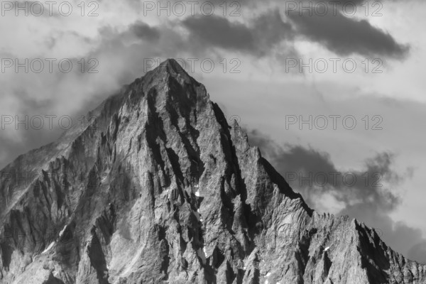 An impressive mountain peak stands in the clouds and reflects the last rays of sunlight until dusk. The texture of the rocks stands out in the soft light. Grachen, Viege, Valais, Switzerland