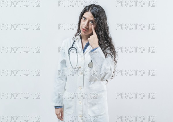 Suspicious female doctor looking you isolated. Suspicious young doctor pointing at eye, isolated