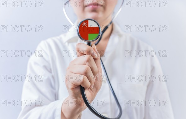 Female doctor holding stethoscope with Oman flag. National health system of Oman