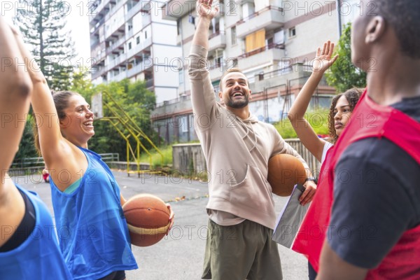 Basketball coach holding a ball under his arm and raising his hand while explaining game strategy to team players on an outdoor court, fostering teamwork and motivation