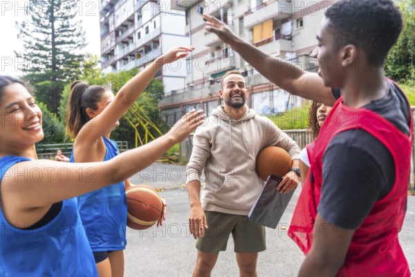 Group of happy basketball players giving high five to their coach after training session on outdoor court, celebrating teamwork and success