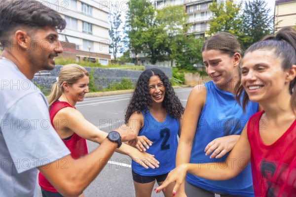 Mixed basketball team celebrating victory after match, putting their hands together, expressing joy and teamwork, outdoors in urban environment