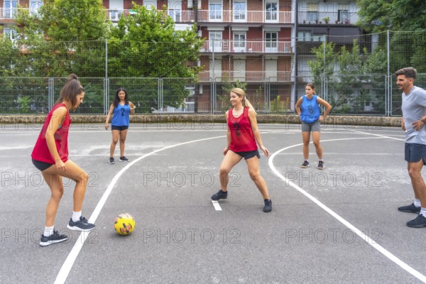 Female soccer players in red and blue jerseys kicking a yellow soccer ball during a friendly outdoor match, highlighting teamwork and athleticism in a neighborhood setting
