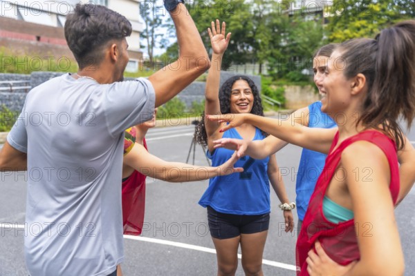 Group of happy basketball players in sportswear celebrating victory, giving high five to each other during training session on outdoor court