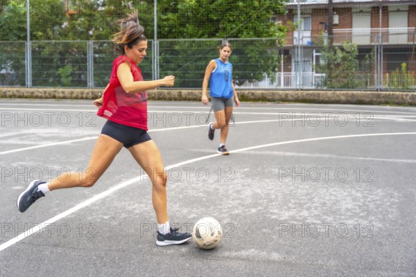 Two women athletes playing soccer on an outdoor court are passing the ball to each other, showcasing their athleticism and teamwork in an urban environment