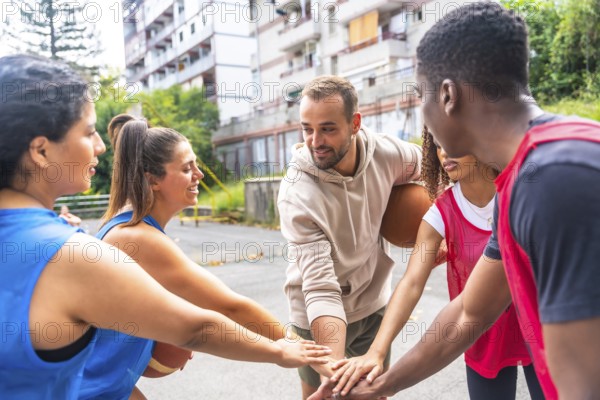 Smiling basketball players joining hands in a huddle before a street match, showcasing teamwork and sportsmanship in an energetic urban environment filled with enthusiasm