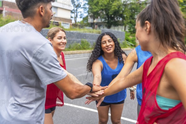 Five smiling soccer players are joining hands before a match, showing their team spirit and motivation on a sunny day in an urban environment