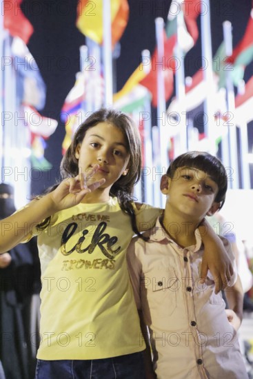 Visitors take souvenir photos at the central square of the Damascus International Fair, with the flags of 22 participating countries displayed in the background. The fair, held after the fall of Assad's regime, drew large crowds exploring cultural and economic exhibitions, Damascus, Damascus, Syria