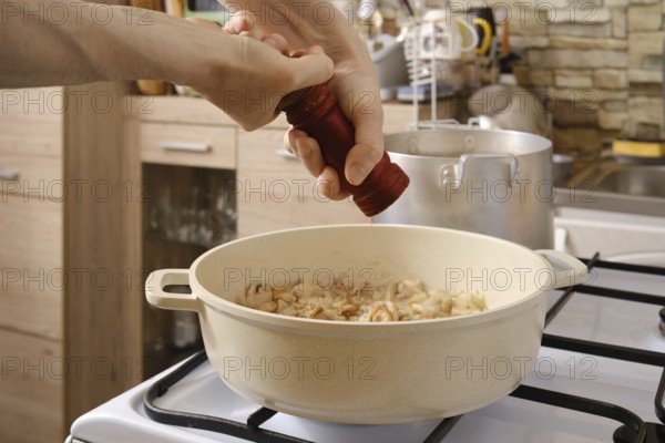 Adding ground pepper in sliced mushrooms roasted in a pot on the stove in the kitchen