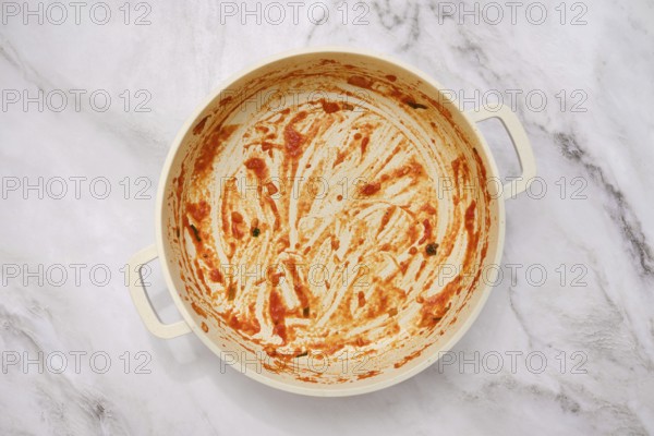 A well-used cooking empty pan on a marble countertop, showing remnants of a vibrant tomato sauce. It hints at a delicious homemade pasta recipe recently enjoyed and savored