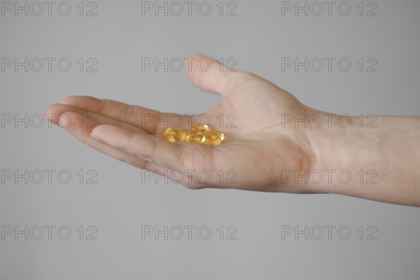 A person extends a hand, showcasing multiple yellow capsules resting on their open palm. The neutral background emphasizes the details of the capsules, highlighting their color and shape