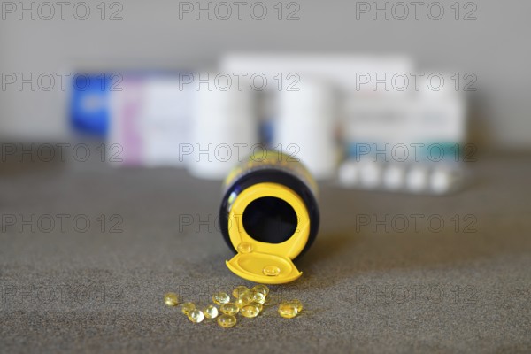Yellow gel capsules are scattered on a grey surface, with a container tipped over