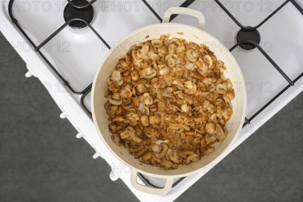 Top view of golden champignon mushrooms fried in oil in a frying pan on the stove in the kitchen