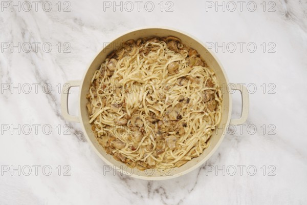 Overhead view of double handled pot with cooked noodles and creamy mushroom sauce on a marble kitchen surface