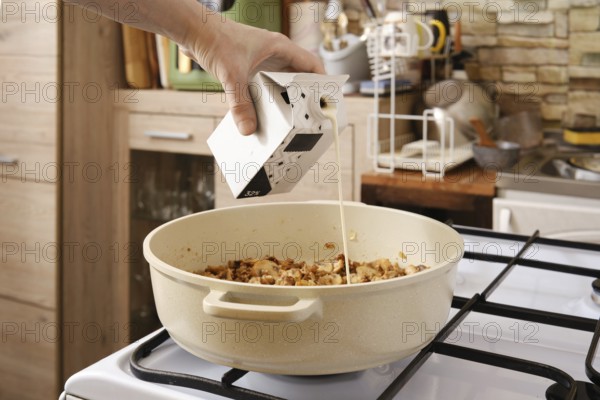 A hand pours cream over roasted mushrooms in a pot on the stove