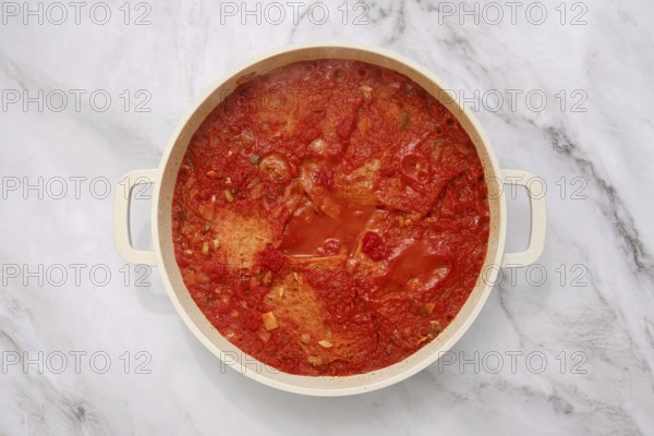 Classic Italian tomato and stale bread soup in cast-iron pot on a marble countertop, overhead view