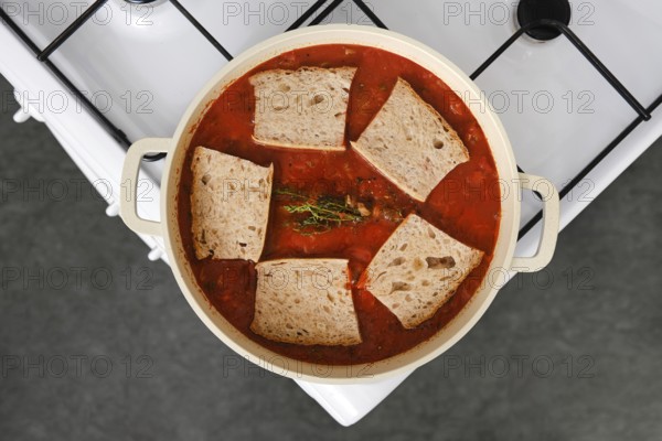 Overhead view of pot of pappa al pomodoro on a stove, filled with a vibrant red tomato broth and chunks of stale bread soaking up the flavours