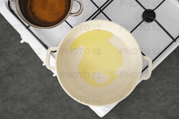 Cooking oil is poured into a frying pan on a stovetop. A pot with vegetable stock sits nearby, indicating preparation of a flavourful dish