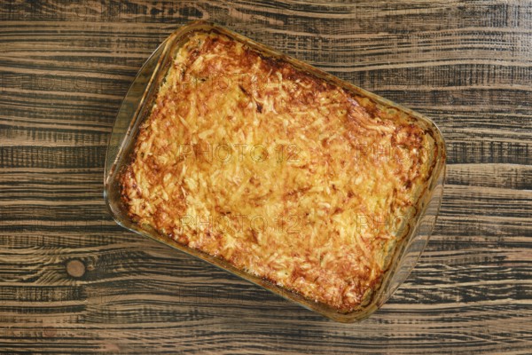 A delicious loaded baked potato casserole sits in a glass dish on a rustic wooden table. The casserole is golden brown and features layers of potatoes, cheese, and toppings, ideal for any gathering