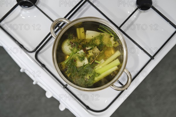 A pot with fresh vegetables boiling on a stove in a contemporary kitchen. Ingredients include celery, onion and herbs, showcasing a healthy cooking process