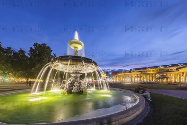 Evening atmosphere at Schlossplatz Stuttgart. View of the Königstraße pedestrian zone and the Königsbau. Illuminated fountain bowl at the fountain. Stuttgart, Baden-Württemberg, Germany