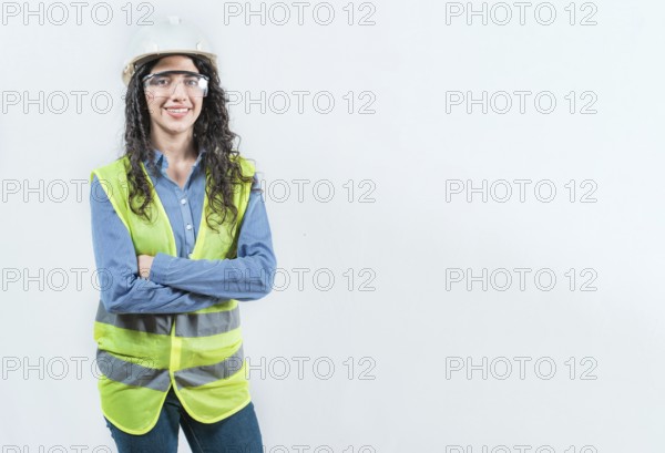 Portrait of smiling female engineer with arms crossed isolated. Young female engineer with helmet and vest looking at camera isolated