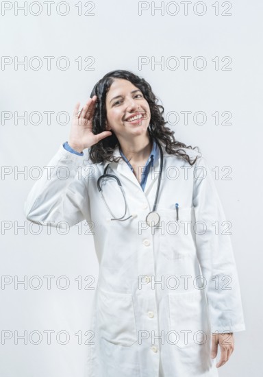 Doctor with hand on ear listening to a rumor, isolated. Latin female doctor hearing a rumor, looking at the camera