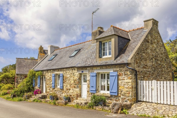 Old idyllic stone cottage with blue shutters and blooming flowers at the house wall by a road in the French countryside, Crozon Peninsula, Bretagne, France