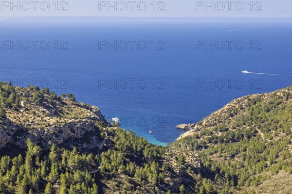 Scenics view at a sea bay with boats from a mountain with green forest and a seascape view to the horizon on the mediterranean sea a sunny summer day, Mallorca, Spain