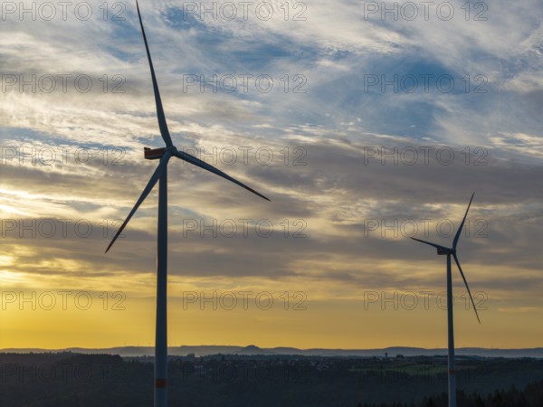 Two wind turbines turn under the early, dramatically lit clouds of a new day, near Schorndorf, Remstal, Rems-Murr-Kreis, Baden-Württemberg, Germany