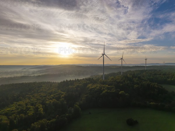 Wind turbines rise above a misty forest at sunrise, a symbol of renewable energy in a peaceful landscape, near Schorndorf, Remstal, Rems-Murr-Kreis, Baden-Württemberg, Germany