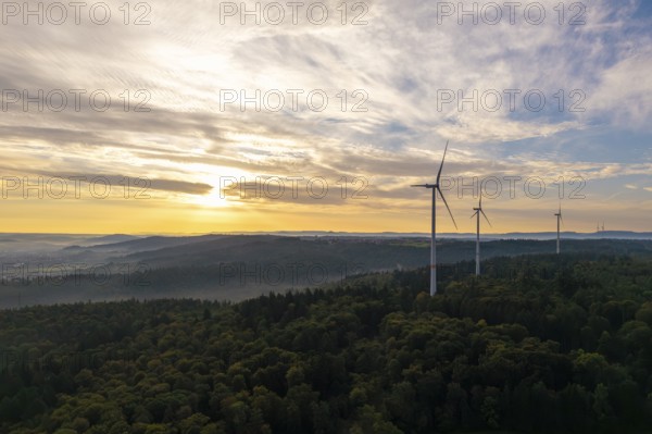 A row of wind turbines overlook a wooded area as the morning fog lifts, near Schorndorf, Rems-Murr district, Rems-Murr-Kreis, Baden-Württemberg, Germany