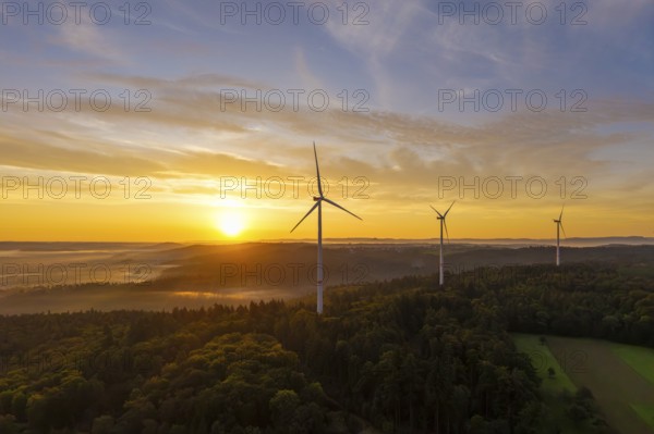 Three wind turbines at sunrise with a golden sky over a forest landscape, near Schorndorf, Rems-Murr district, Rems-Murr-Kreis, Baden-Württemberg, Germany