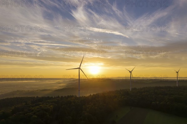 Wind turbines stand still under a soft sunlight illuminating the sky and forest, near Schorndorf, Remstal, Rems-Murr-Kreis, Baden-Württemberg, Germany